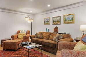 Un salon avec un canapé marron, un fauteuil et un pouf, une table basse et un lampadaire. Trois tableaux encadrés ornent le mur.