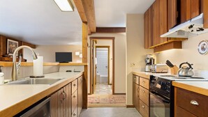 Cocina compacta con armarios de madera, lavavajillas, estufa y pileta.