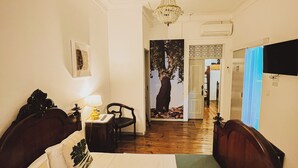 A hotel room with a large bed, a desk with a lamp, a chair, a chandelier, and a painting of a tree. - Very Typical - Alojamento Local (Elvas)