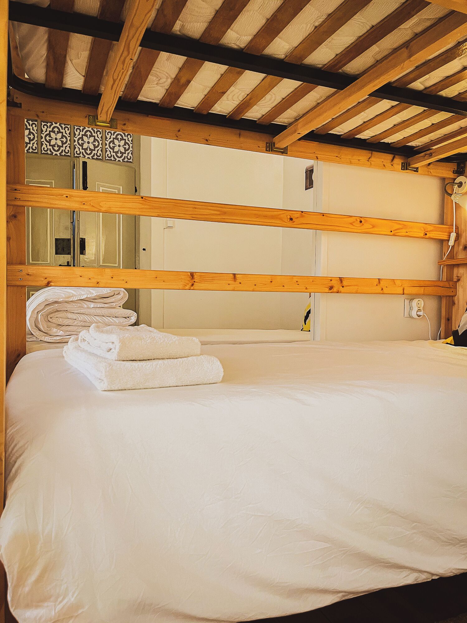 A bunk bed with white bedding and towels, wooden beams, and a tiled wall.