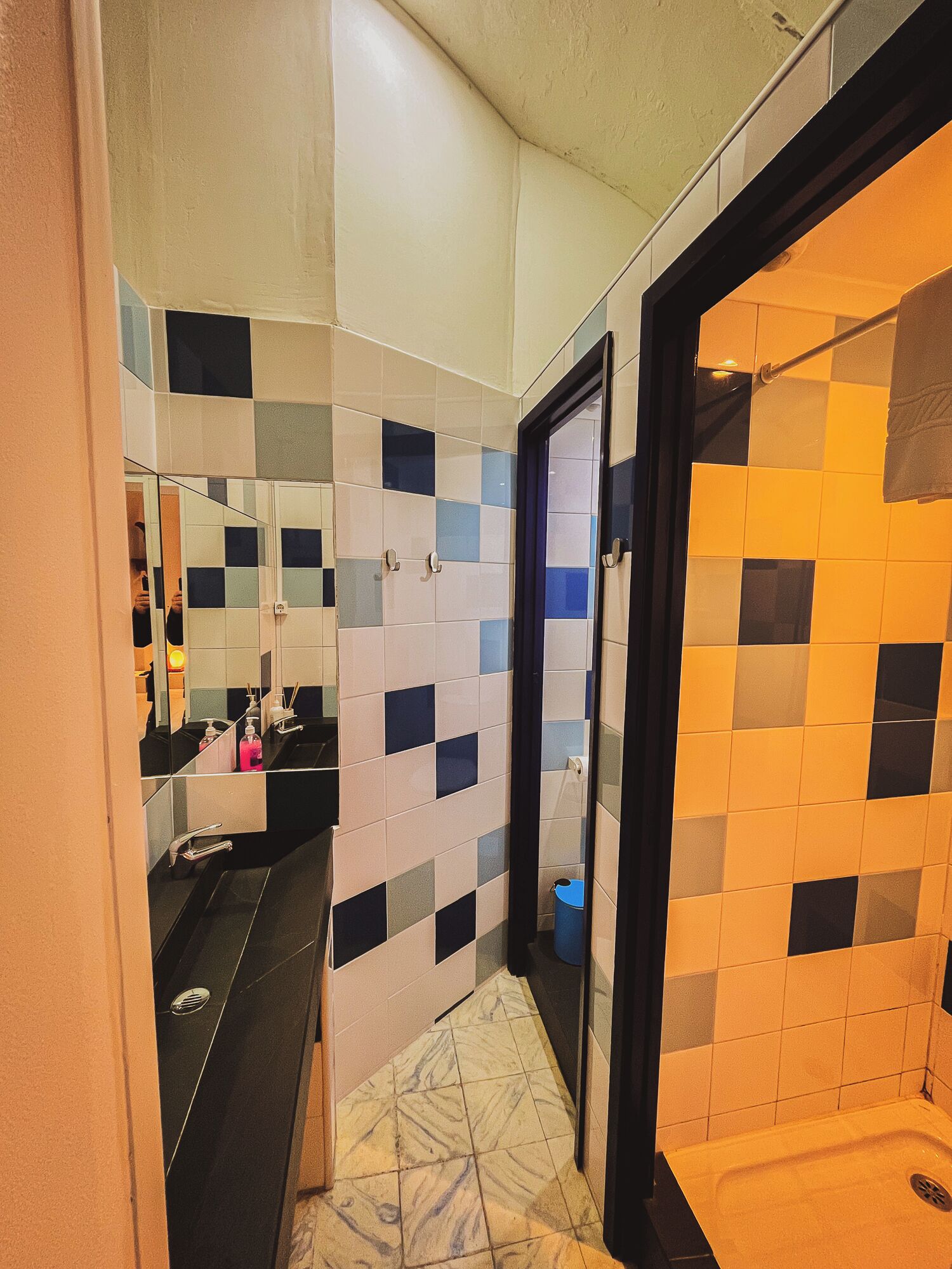 A bathroom with a tiled floor, a sink with a mirror, and a shower area.