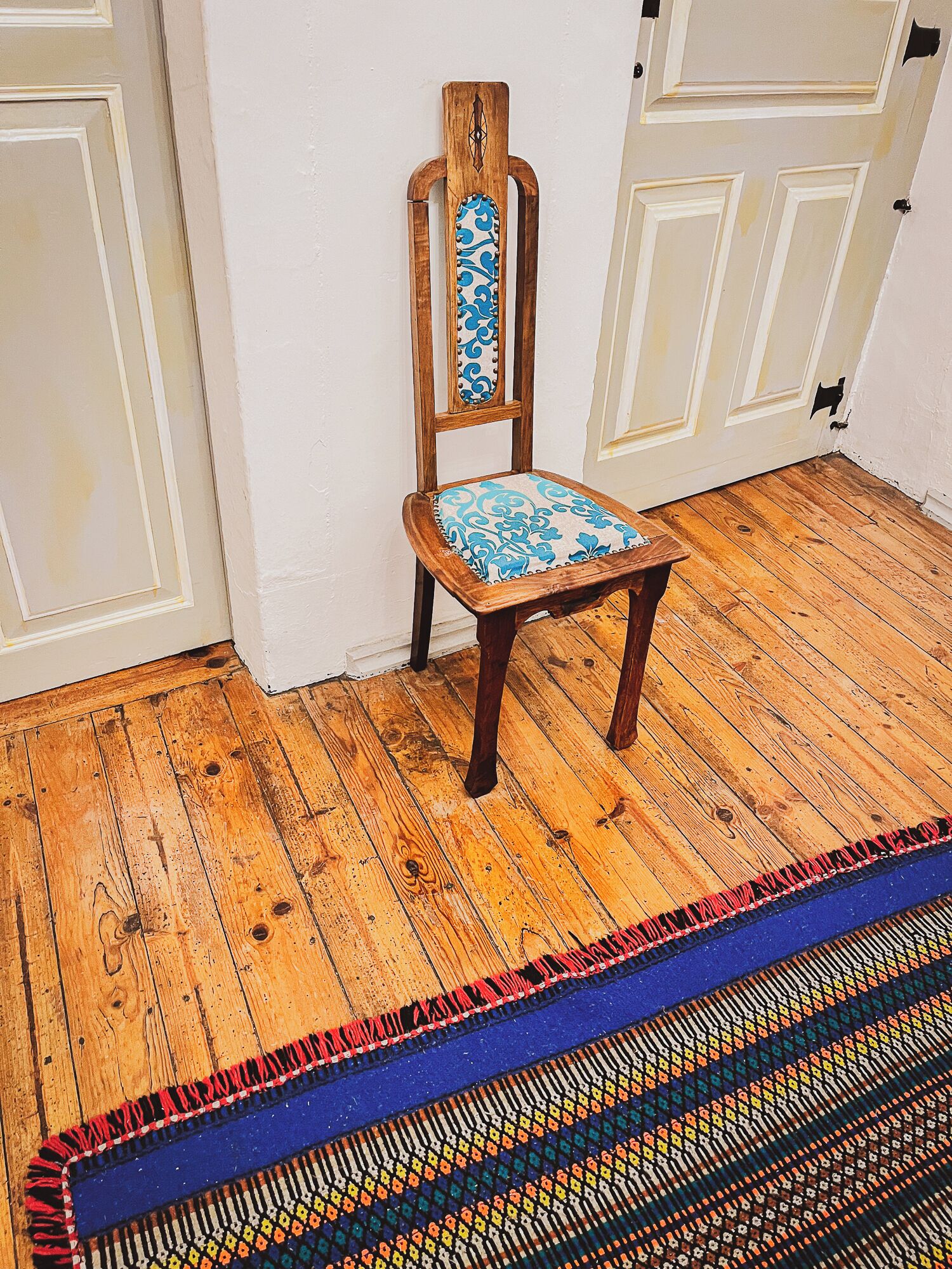 Uma cadeira de madeira com almofada azul estampada em um quarto com piso de madeira e paredes brancas.