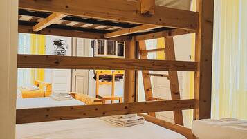 A bunk bed room with wooden beams, a window with yellow curtains, and a small table with a book.