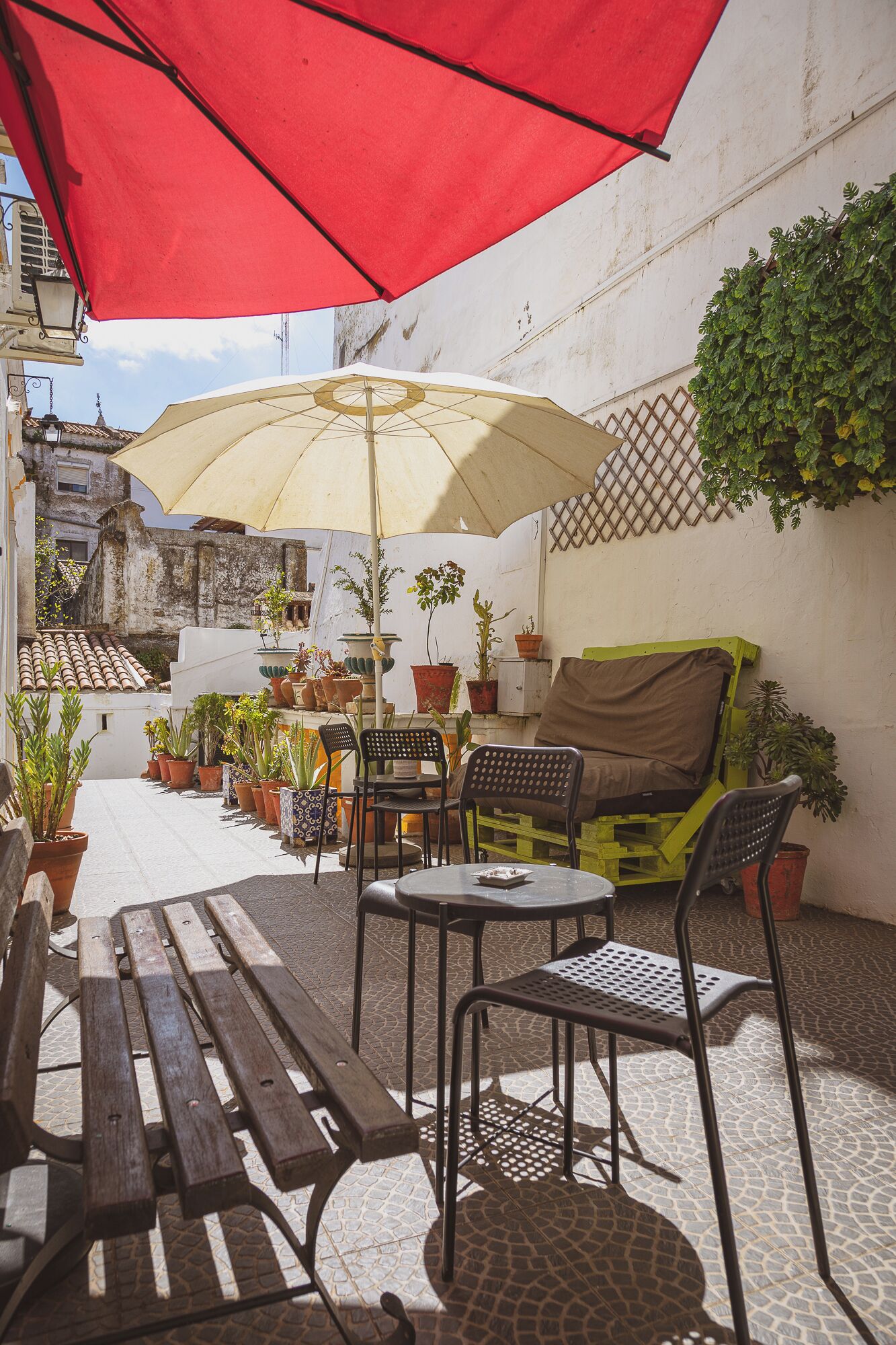 Un patio con un paraguas rojo, uno amarillo y varias plantas en macetas.