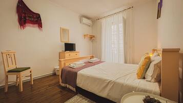 A bedroom with a bed, a chair, a TV, a mirror, and a window with curtains.