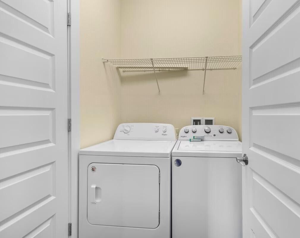 A laundry room with two stacked washers and dryers, a metal drying rack, and a beige wall.