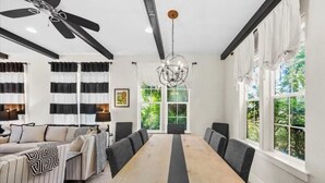 A dining area with a long wooden table, black and white striped curtains, and a ceiling fan. - Villa Soleil Dunes (Miramar Beach)
