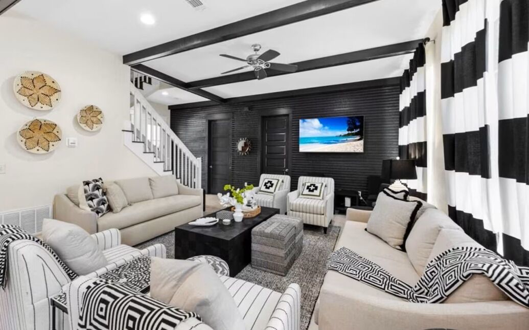 A modern living room with a staircase, a ceiling fan, and a TV on the wall.