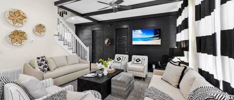 A modern living room with a staircase, a ceiling fan, and a TV on the wall.