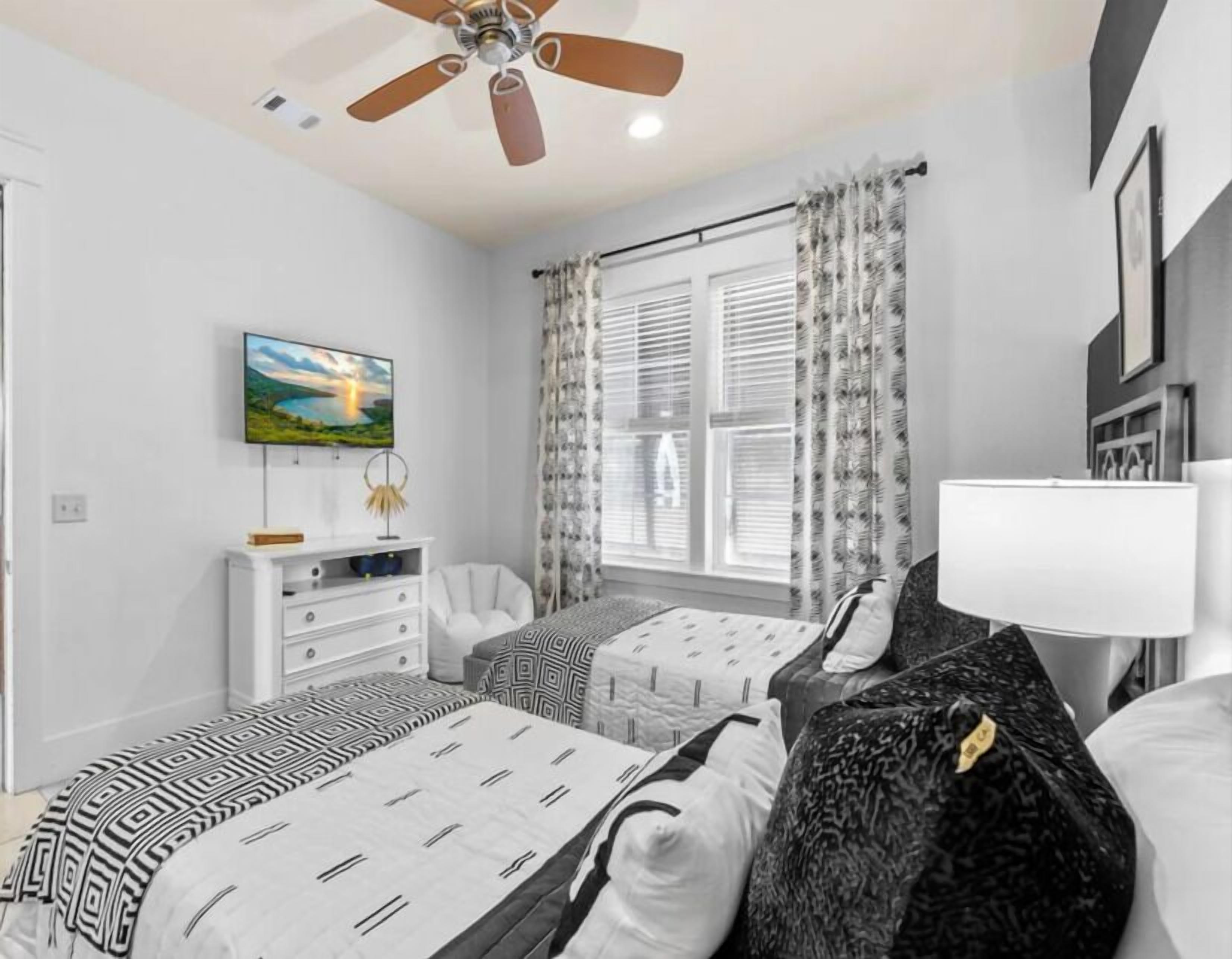 A bedroom with two beds, a ceiling fan, a TV, and a window with curtains.