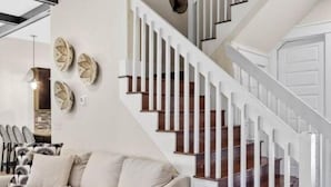 A modern living room with a beige sofa, a black side table, and a staircase with white railings and wooden steps. - Villa Soleil Dunes (Miramar Beach)