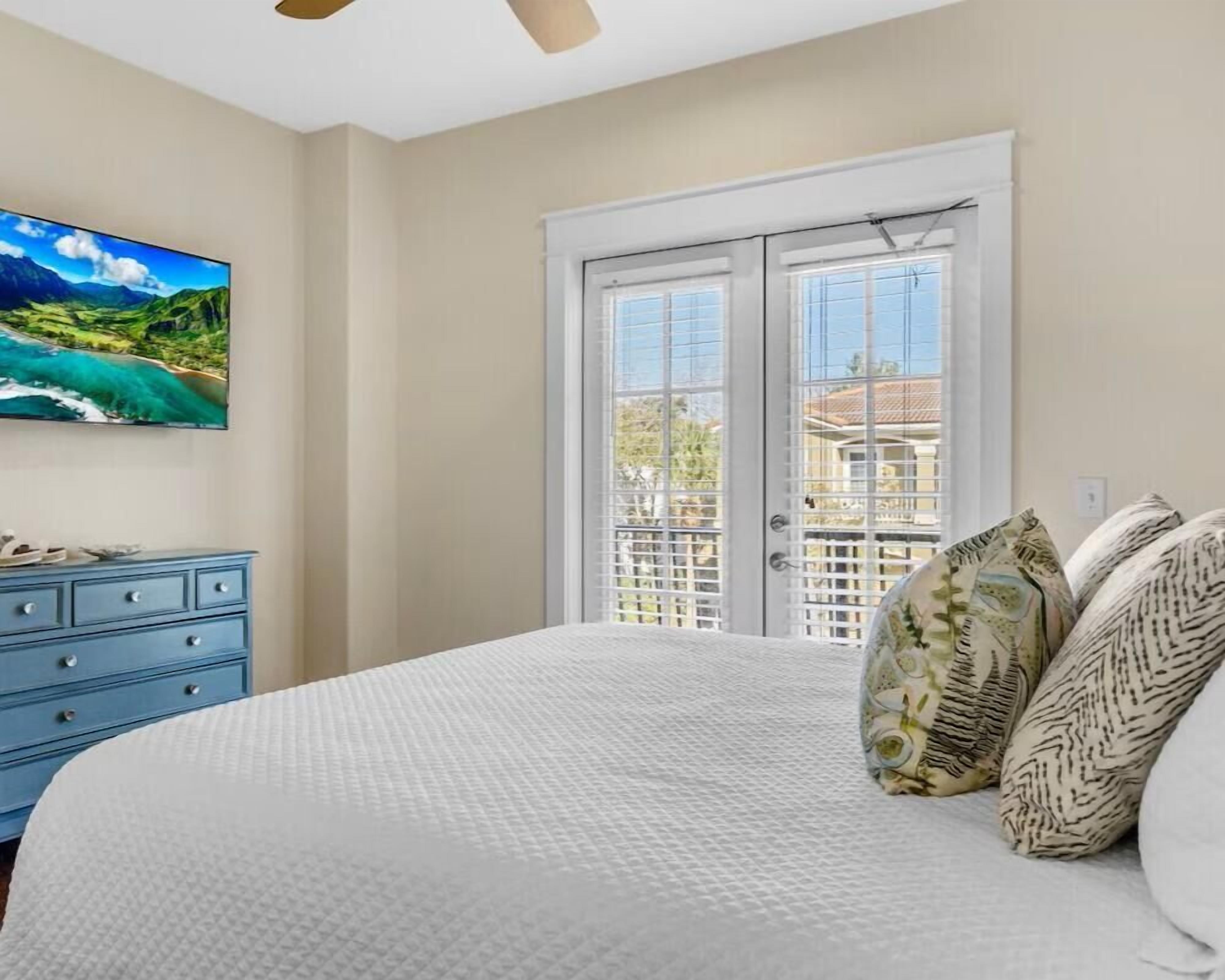A bedroom with a bed, a dresser, a painting, and a door with a view.