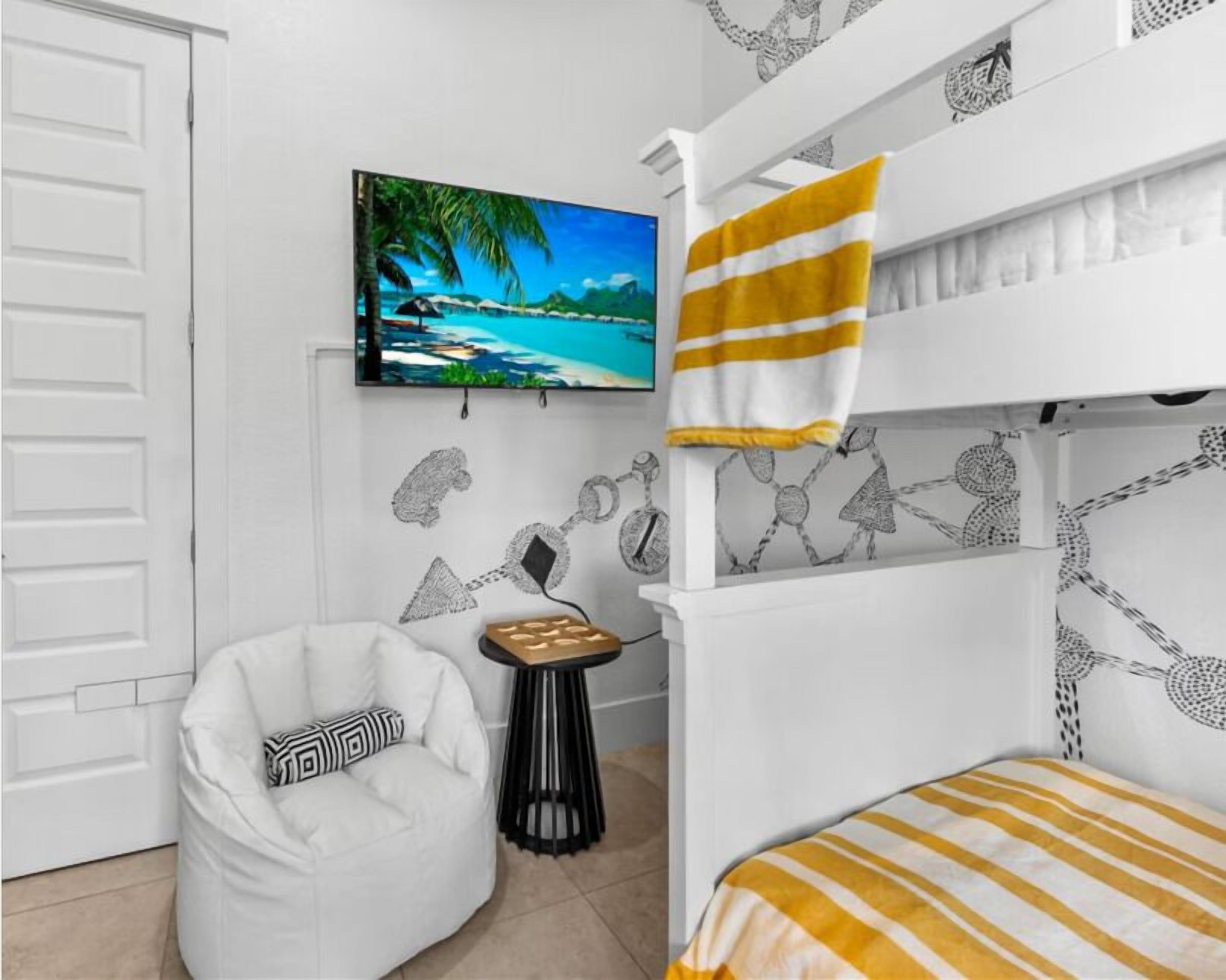 Ein Zimmer mit einem Etagenbett, einem weißen Sessel, einem kleinen Tisch mit einem Gesellschaftsspiel und einem Gemälde, das eine Strandansicht zeigt.