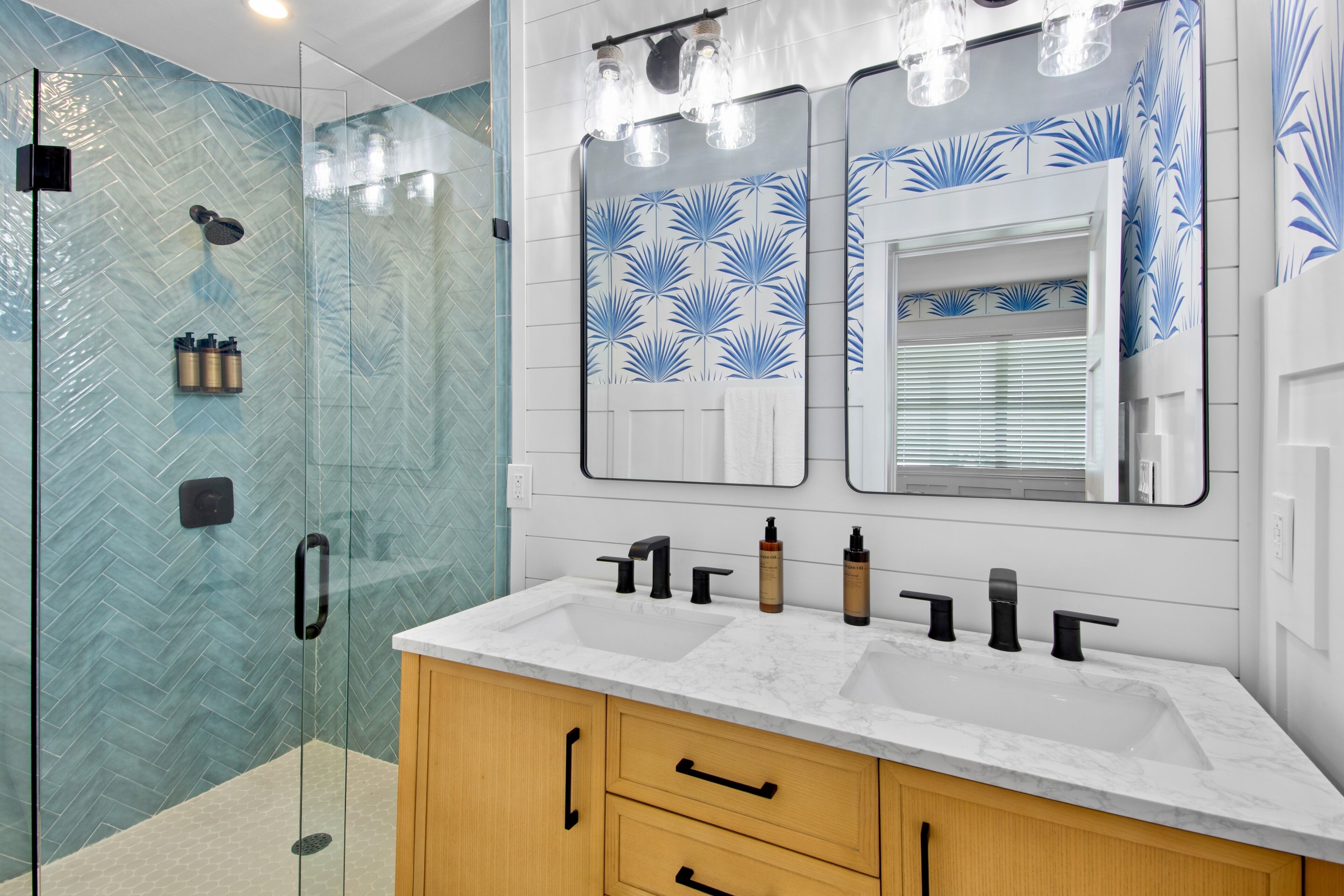 A modern bathroom with a glass shower enclosure, a large mirror, and a marble sink with multiple faucets.