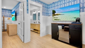 A modern bathroom with a large mirror, a wooden cabinet, and a television mounted on the wall. - Cottages at Siesta Key Inn (Siesta Key)