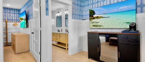 A modern bathroom with a large mirror, a wooden cabinet, and a television mounted on the wall.