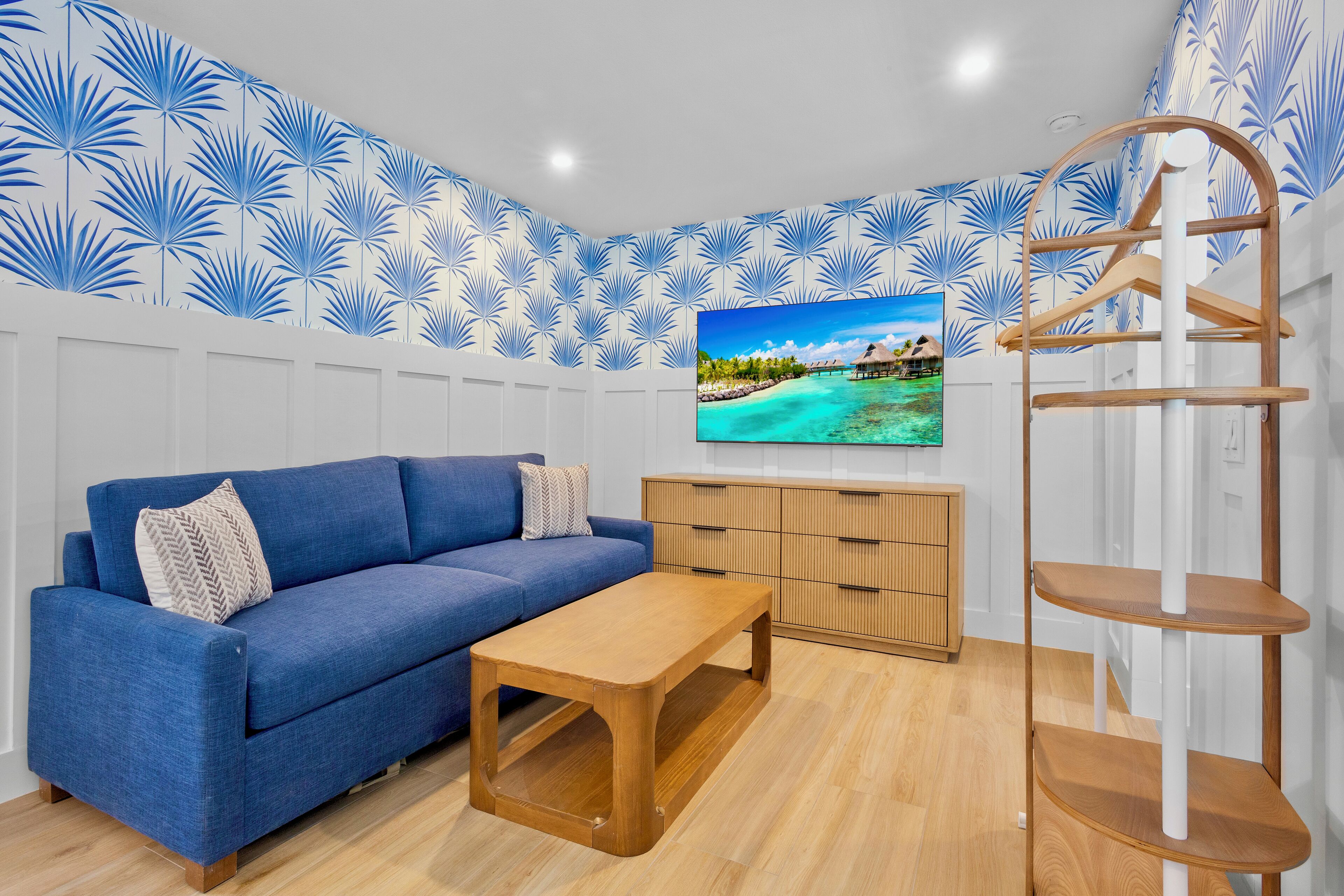 Ein modernes Wohnzimmer mit einem blauen Sofa, einem Holztisch und einem Fernseher an der Wand.