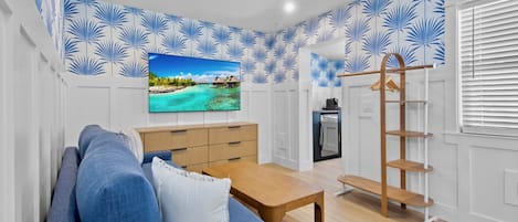 Una sala de estar con un sofá azul, una mesa de centro de madera y un televisor que muestra una playa tropical.