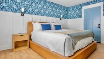 A bedroom with a wooden bed, white bedding, a nightstand, and blue patterned wallpaper.