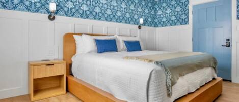 A bedroom with a wooden bed, white bedding, a nightstand, and blue patterned wallpaper.