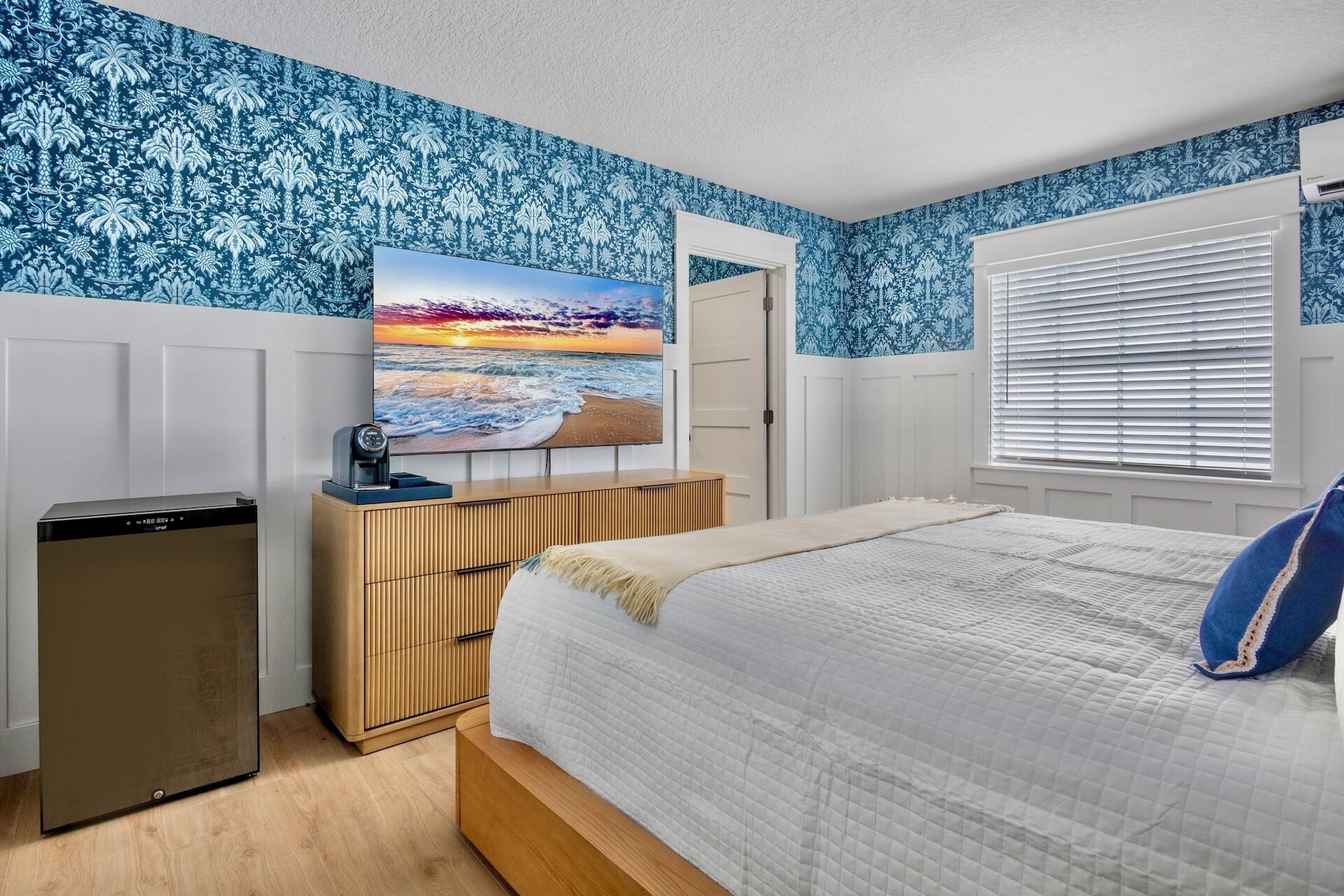 Un dormitorio con cama, cómoda, televisor y ventana con persianas.