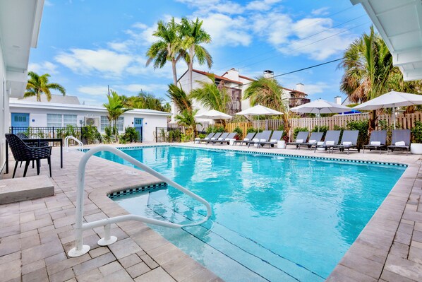 A swimming pool with lounge chairs and umbrellas, surrounded by palm trees and a white building. - Cottages at Siesta Key Inn (Siesta Key)