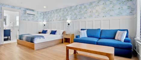A modern bedroom with a bed, a blue sofa, a wooden coffee table, and a wall with floral wallpaper.