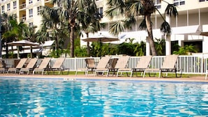 A swimming pool with lounge chairs and umbrellas, surrounded by palm trees and a multi-story building. - Cottages at Siesta Key Inn (Siesta Key)
