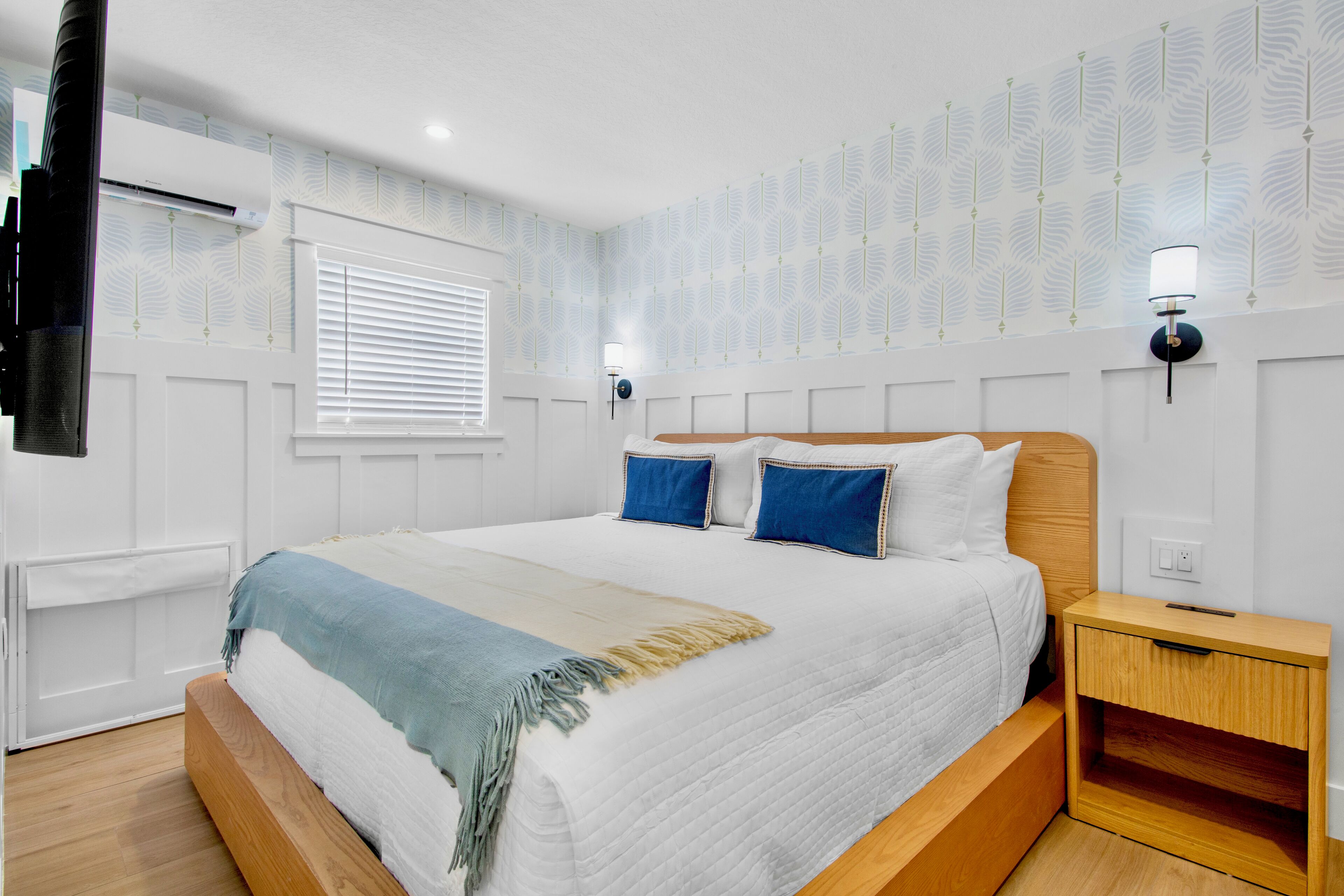 A bedroom with a large bed, a nightstand, a wall-mounted TV, and patterned wallpaper.