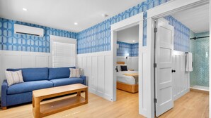 A room with a blue patterned wall, a wooden floor, a blue sofa, a wooden bench, and a bed with a white headboard. - Cottages at Siesta Key Inn (Siesta Key)