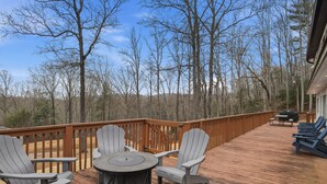 Une terrasse en bois avec des fauteuils Adirondack, une table ronde et un barbecue.