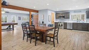 Une cuisine spacieuse équipée d’appareils modernes, un coin repas avec une table et des chaises en bois, et une table de billard à l’arrière-plan.