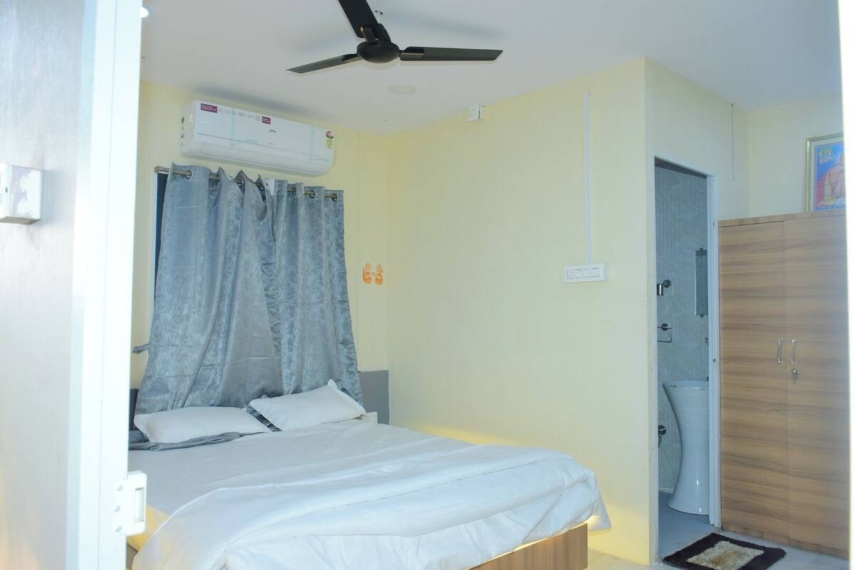Een slaapkamer met een bed, een plafondventilator, een airconditioningapparaat, een deur naar een badkamer en een houten garderobe.