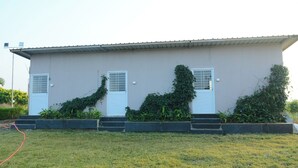 Un bâtiment à deux étages, doté d’un toit plat et d’une façade beige. Il y a deux portes blanches avec des panneaux de verre, chacune surmontée d’une petite fenêtre. Le bâtiment présente un design simple et moderne, sans fenêtres apparentes sur le côté faisant face à l’observateur.