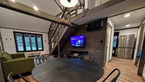 A modern kitchen with a built-in refrigerator, a dining area with a round table and chairs, and a staircase leading to an upper level. - Hummingbird Hollow • Hot Tub • Private Forest Stay (Irvine)