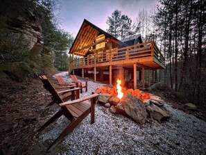 Una cabaña con terraza de madera, mobiliario exterior y una fogata.
