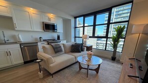 Ein modernes Wohnzimmer mit einer Couch, einem Couchtisch und Blick auf die Stadt durch große Fenster.