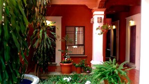 A courtyard with a red building, potted plants, and a small fountain. - HOTEL MAELA (Oaxaca)