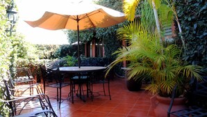 An outdoor patio with a round table and chairs, surrounded by potted plants and a large umbrella. - HOTEL MAELA (Oaxaca)