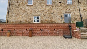A stone building with a brick lower section, two windows, a door, and a small step leading to the entrance. - The Granary (Durham)