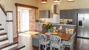 A modern kitchen with a dining area, featuring a wooden staircase, grey cabinets, and a stainless steel refrigerator. - The Granary (Durham)