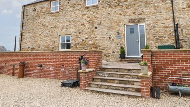 A stone building with a brick entrance, a door, and a small window. - The Granary (Durham)