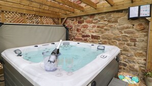 A hot tub with a bottle of champagne and two glasses, set against a stone wall with a wooden pergola overhead. - The Granary (Durham)