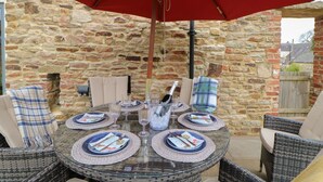 A round glass table with a red umbrella overhead, set with plates, glasses, and cutlery. - The Granary (Durham)