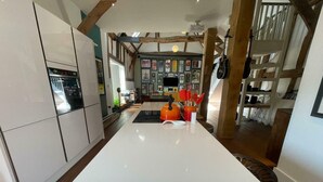 Une cuisine moderne dotée d’un îlot central, de poutres en bois et d’un mur décoré de tableaux encadrés.