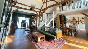 Un loft spacieux avec des poutres apparentes, un canapé vert, une table basse en bois et un escalier menant à un niveau supérieur.