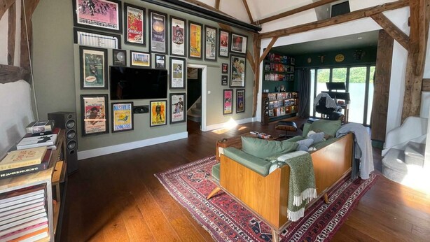Un salon spacieux avec un plafond en bois, un canapé vert, un téléviseur et un mur décoré d’affiches encadrées.