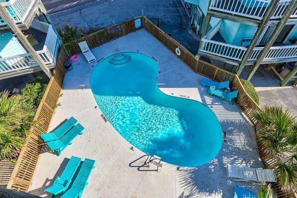 A unique, kidney-shaped swimming pool surrounded by wooden fences and blue lounge chairs.