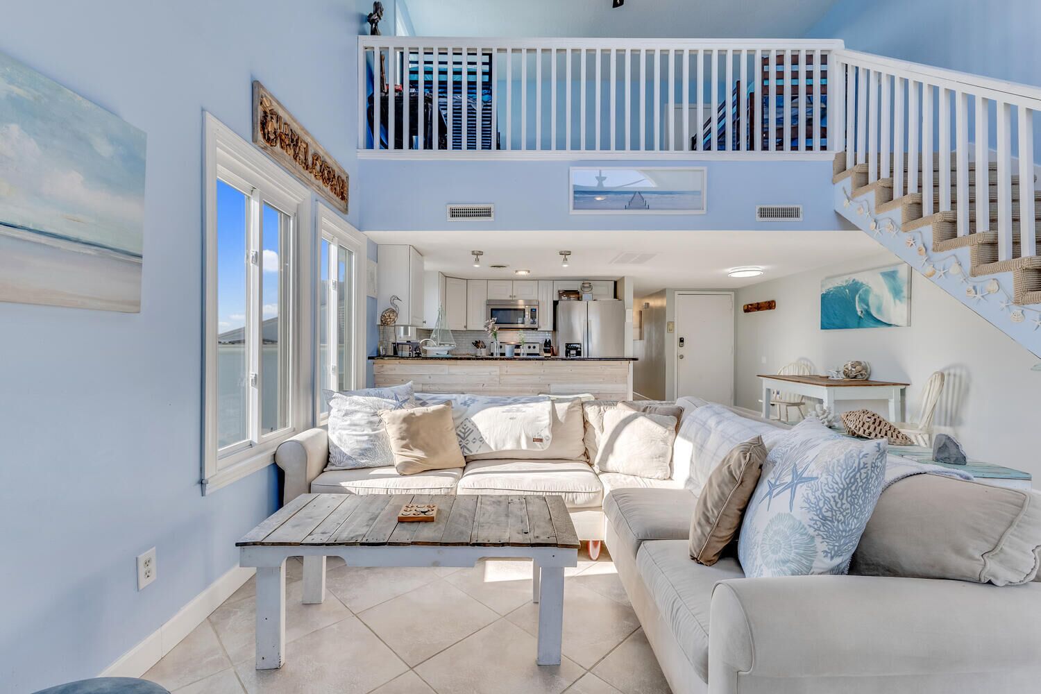 A spacious living area with a large sofa, a coffee table, and a view of the kitchen and balcony.