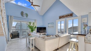 A spacious living room with a large sofa, a TV, and a balcony with a view. - Paradise Found - Pet friendly home with Ocean & Marsh Views! (Carolina Beach)